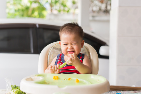 the baby learns to eat by himself. he can use spoon well. so he is very happy (focus at his face)の写真素材