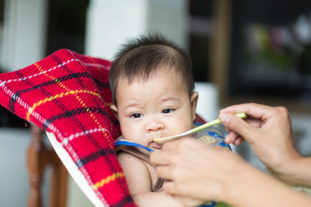 the baby learns to eat by himself. he can use spoon well. so he is very happy (focus at his face)の写真素材
