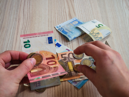 Hands taking euro banknotes and coins on wooden background.の写真素材