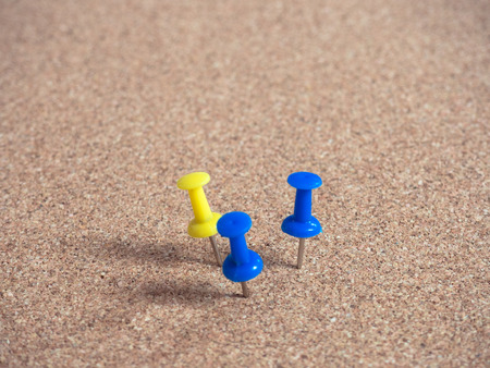 Blue and yellow pins on brown cork board.