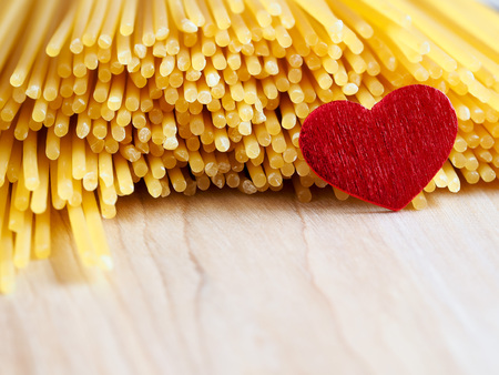 Raw spaghetti with red heart on a wooden bakground - close upの写真素材