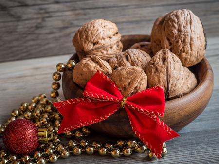 Wooden bowl full of tasty walnuts, big red bow, gold ornament and golden christmas chain made from...