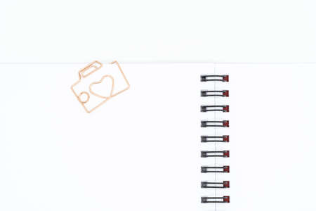 Close up of paper clip in shape of camera with heart on blank spiral notebook isolated on white backgroundの写真素材