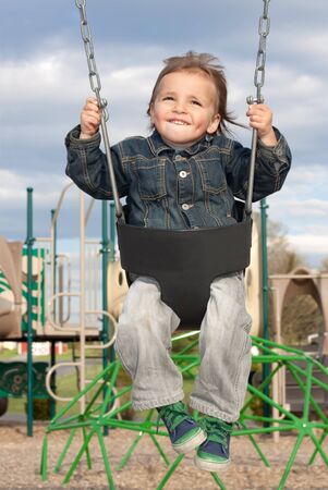 A young boy swinging at the playground on a beautiful spring day の写真素材