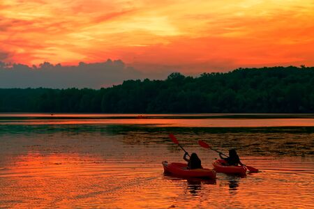 A young couple paddle kayaks on a lake at sunset.の写真素材