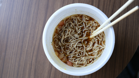 instant noodles on white foam cup and chopsticks on wood table