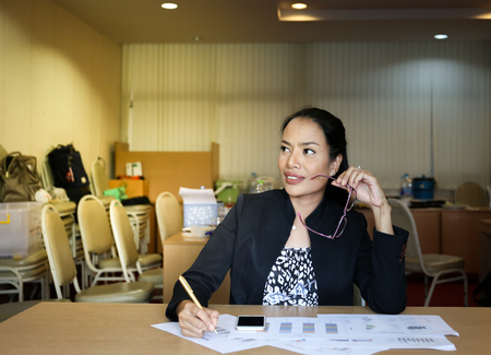 working woman who wear suit is holding glasses with left hand look confident and has ideaの写真素材