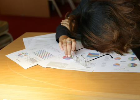 woman sleep and left glasses on the wood working desk above business charts paperの写真素材