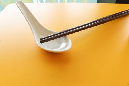 dark brown chopstick on white spoon on yellow table