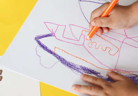 kid draws something with orange color pencil on white paperの写真素材