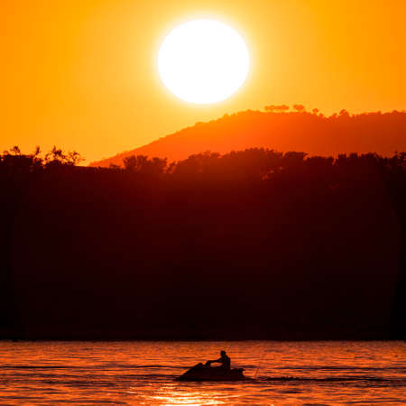 A jet ski on the sea with an orange sunset in the backgroundの写真素材