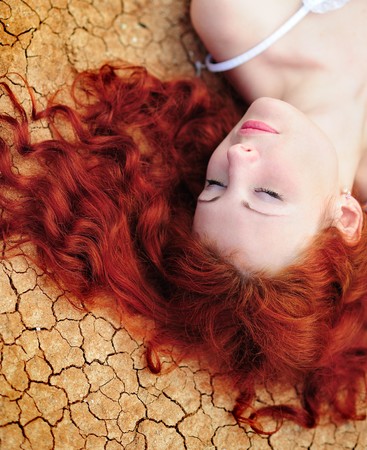 Beauutiful young woman with red hair on the dried up groundの写真素材