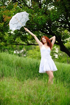 Cute young redhead female standing on grass field at the park with umbrellaの写真素材