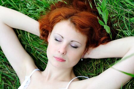 Cute young redhead female lying on grass field at the park の写真素材