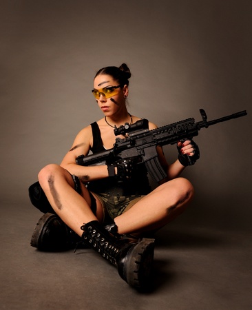 Sexy army woman posing with weapon, on gray background.の写真素材