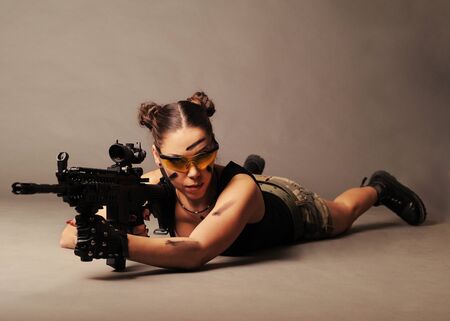 Sexy army woman posing with weapon, on gray background.の写真素材