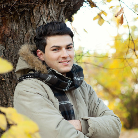 Young smiling man portrait standing in front of an autumn tree.の写真素材