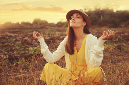 Young attractive female meditate sitting on a deadwood autumn field.
