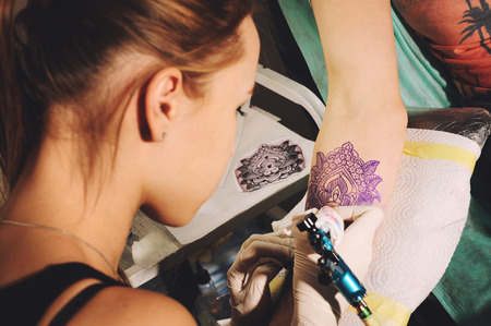Girl tattoo artist makes tattoo on a hand against purplish blue likeness of a future tattoo using a sketch.の写真素材