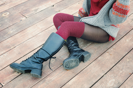 Female legs dressed in knee high boots and knitted stockings, woman sitting on a wooden planking, winter outdoorの写真素材
