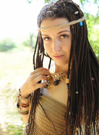 Beautiful sexy boho style woman with dreadlocks portrait, looking at camera, against sunny summer...