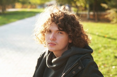 Portrait of a young depressed man in autumn park, looking at cameraの写真素材