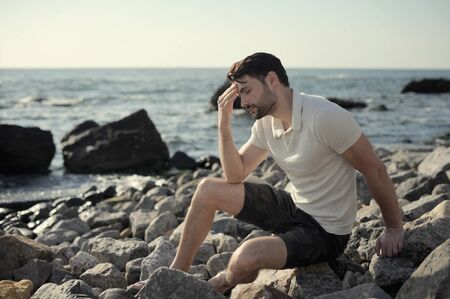 Alone sad man sitting on a sea beach, outdoor