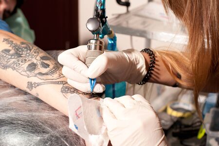 Girl tattoo artist portrait during creation tattoo on a man`s hand under the lamp light, no faceの写真素材