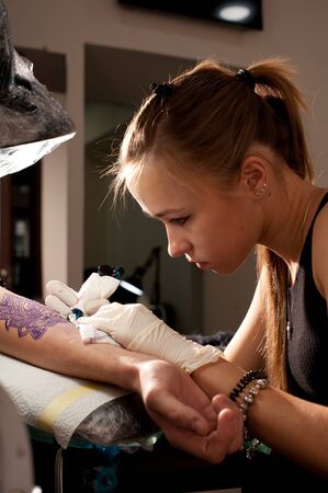 Girl tattoo artist makes tattoo on a hand against purplish blue likeness of a future tattoo using a sketch.の写真素材
