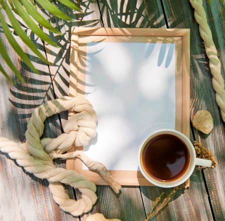 Mock up with empty wooden frame, rope and cup of coffee, outdoor summer photo, marine style, palm shadowsの写真素材