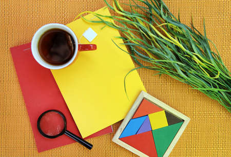 Flat lay top view outdoor photo with bright red and yellow notebooks, tea mug, magnifier and...