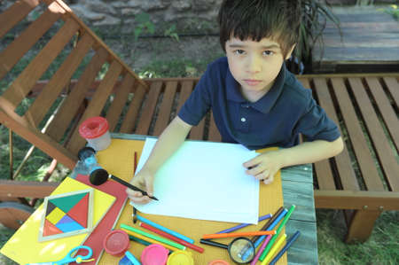 Child boy have a leisure drawing at the backyard, looking at camera