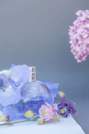 Violet circle perfume bottle on gray backdrop with flowers