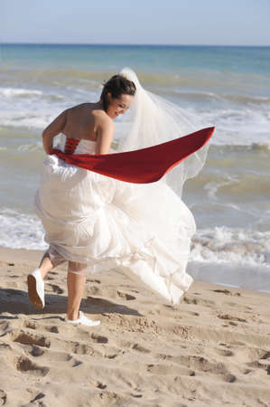 Happy funny young bride walking on a sea beachの写真素材