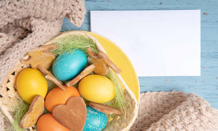 Easter background with colored eggs and cookies, empty white list, flat lay
