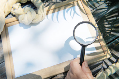 Mock up with empty wooden frame, rope and magnifier in a hand, outdoor summer photo, marine style, palm shadowsの写真素材