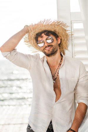 Handsome man dressed in straw hat and sun glasses, outdoor portrait against sea landscapeの写真素材
