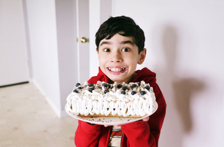 Cute happy boy holding homemade blueberry pie with white creamの写真素材