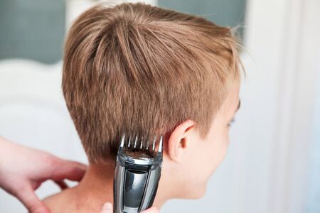 Blond boy gets haircut at home during quarantine isolation. Father cuts his with hair clipper. Stay home conceptの写真素材