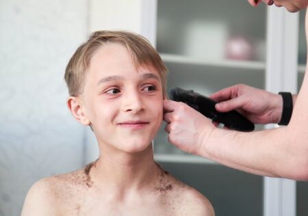 Blond boy gets haircut at home during quarantine isolation. Father cuts his with hair clipper. Stay home conceptの写真素材