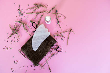 Pink Gua Sha massage tool made of rose quartz on the pink background with dried lavender flowers.の写真素材