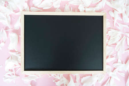 Black board for notes on the pink background with white peonies petalsの写真素材