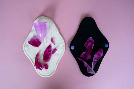 Purpure menstrual cup and reusable cotton cloth woman pads on the pink background with red peonies...