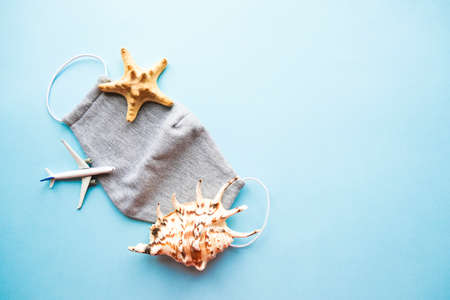 Medical mask, seashells and plane on a blue background. Protection from COVID-19 concept. Flatlay.の写真素材