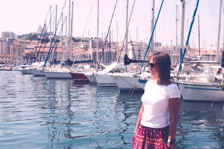Portrait of young woman standing on the pier in harbor with yachts on the background.の写真素材