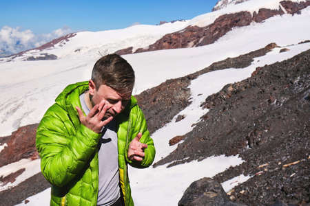 A man tourist in the mountains soars his face with spf cream