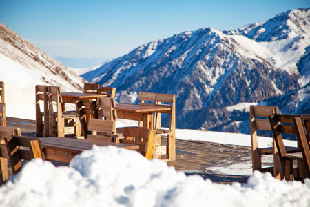 Outdoor restaurant terrace on top of a snowy mountain with wooden tables and chairsの写真素材