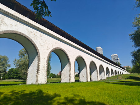 A view of a historic aqueduct featuring multiple arches, set against modern city buildings and lush greenery.の写真素材