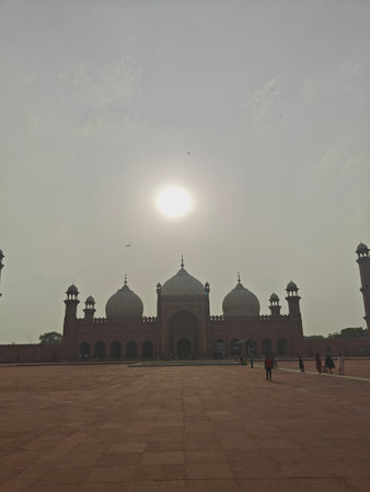 The iconic Badshahi Mosque in Lahore, Pakistan, silhouetted against the sunlit sky, showcasing its grand domes, minarets, and expansive courtyard under a serene atmosphere.の写真素材