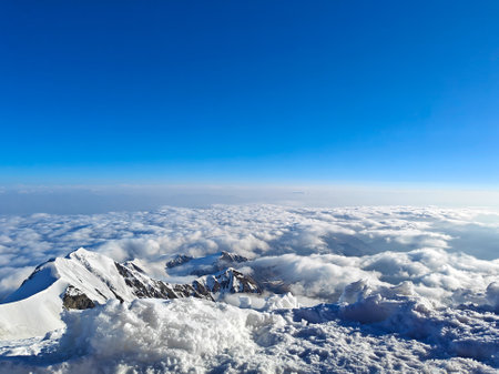Breathtaking panoramic view of snow-covered peaks rising above thick clouds under a bright blue sky.